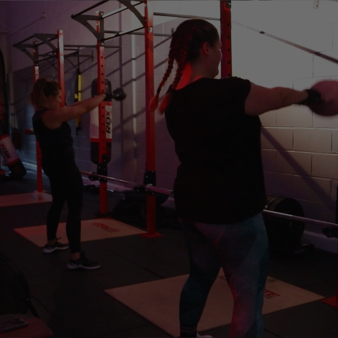 two girls swinging kettlebells at a small group personal training session